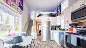 A modern kitchen with a built-in oven, microwave, and dishwasher. There is a dining area with a table and chairs, and a staircase leading to an upper level.