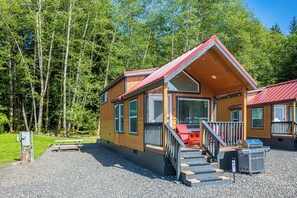A cabin with a red roof, a porch, and a gravel driveway.