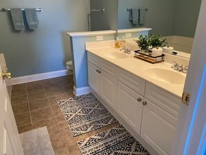 A bathroom with two sinks, a toilet, and a shower. There are towels hanging on a rack, a rug on the floor, and a plant on the counter. - Barefoot Bungalow- 5 minutes from the beach, shops, music and restaurants! (North Myrtle Beach)
