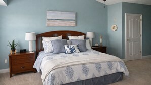 Een slaapkamer met een bed, nachtkastjes, een plafondventilator, een aan de muur hangend schilderij en een deur.