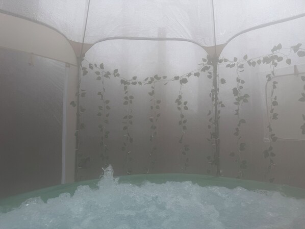 A room with a bathtub, a shower, and a wall with hanging vines.