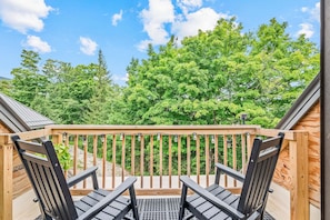 A wooden deck with two chairs and a railing, overlooking a forested area. - Fully Renovated Upscale Condo, Walk to Snowshed, Amenities Downstairs (Killington)