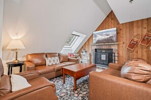 Un salon chaleureux de style loft, avec une cheminée, des canapés en cuir, une table basse et une lampe.