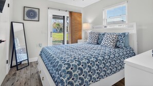 A bedroom with a bed, a ceiling fan, a window with blinds, a door, and a mirror.