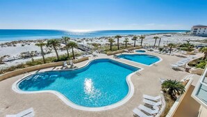 Et poolområde med to pools, liggestole og udsigt til strand og hav.