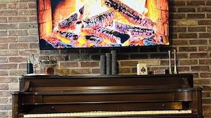Un televisor montado en una pared de ladrillo muestra un fuego. Abajo, hay un piano con un banco delante.
