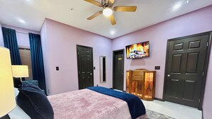 Un dormitorio con cama, ventilador de techo, televisor y puerta.