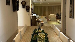 A dining area with a long wooden table, cushioned chairs, and a Christmas tree centerpiece. - Luxury Apartment in Ondina (Carnival - Barra-Ondina Circuit) (Salvador)