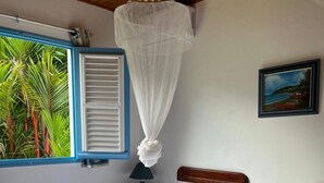Une chambre avec deux lits, une fenêtre avec des volets bleus, un ventilateur de plafond et un tableau accroché au mur.