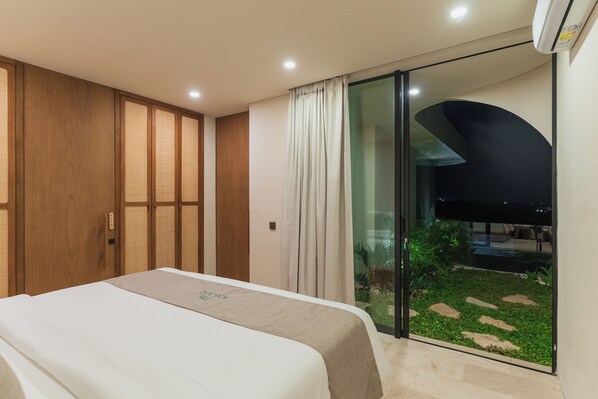 A modern bedroom with a bed, a wardrobe, and a sliding glass door leading to a balcony with a garden view. - Villa Kalani Spirit by Alfred in Bali (Pecatu)