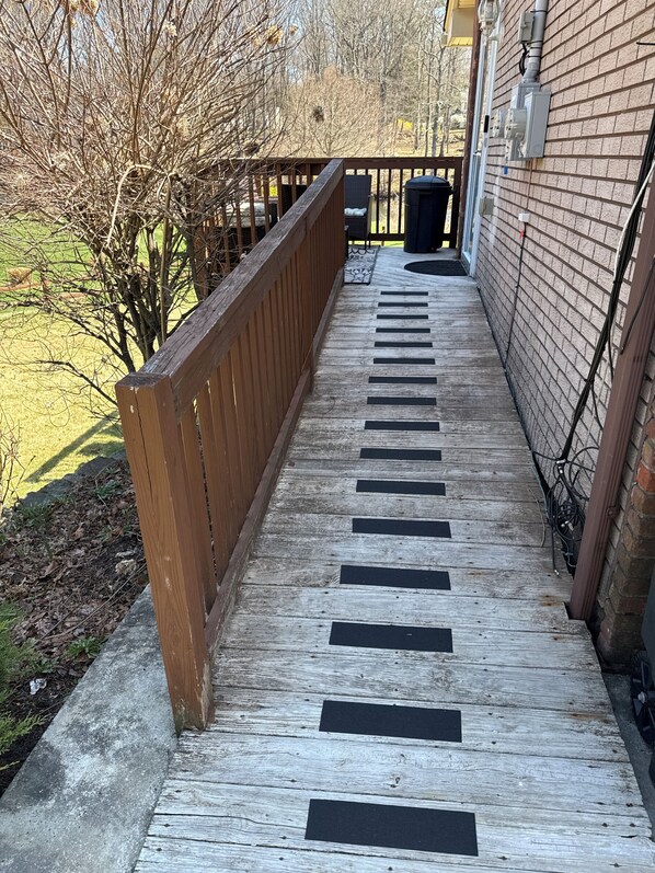 Een houten terras met een hekwerk, dat leidt naar een gebouw met een bakstenen gevel.