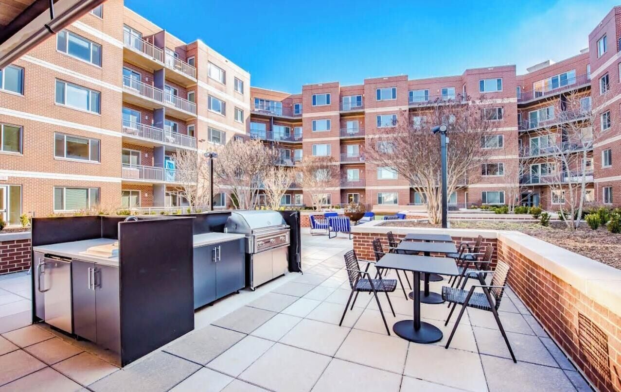 A patio area with a grill, outdoor seating, and a view of apartment buildings.