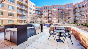 Un patio con una parrilla, mobiliario exterior y vistas a edificios de apartamentos.