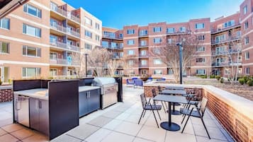 A patio area with a grill, outdoor seating, and a view of apartment buildings.