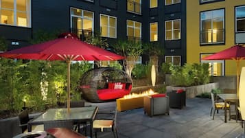 An outdoor patio area with seating and a fire feature, surrounded by buildings with illuminated windows.