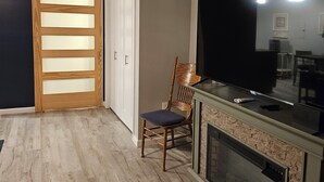 A room with a wooden floor, a sliding door with frosted glass panels, a wooden chair, a flat-screen TV, and a fireplace. - Modern Handicapped Accessible Studio Apartment In-Law suite (Harrison)