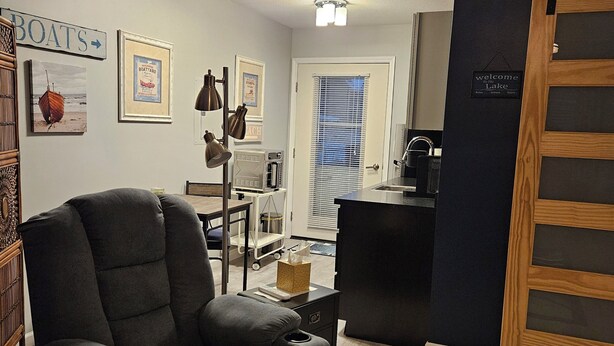 A living room with a grey sofa, a coffee machine, a framed picture of a boat, and a sign that says "welcome to Lake". - Modern Handicapped Accessible Studio Apartment In-Law suite (Harrison)