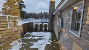 A wooden deck with a metal chair, a fenced area with snow patches, and a building with a window and light fixture. - Modern Handicapped Accessible Studio Apartment In-Law suite (Harrison)