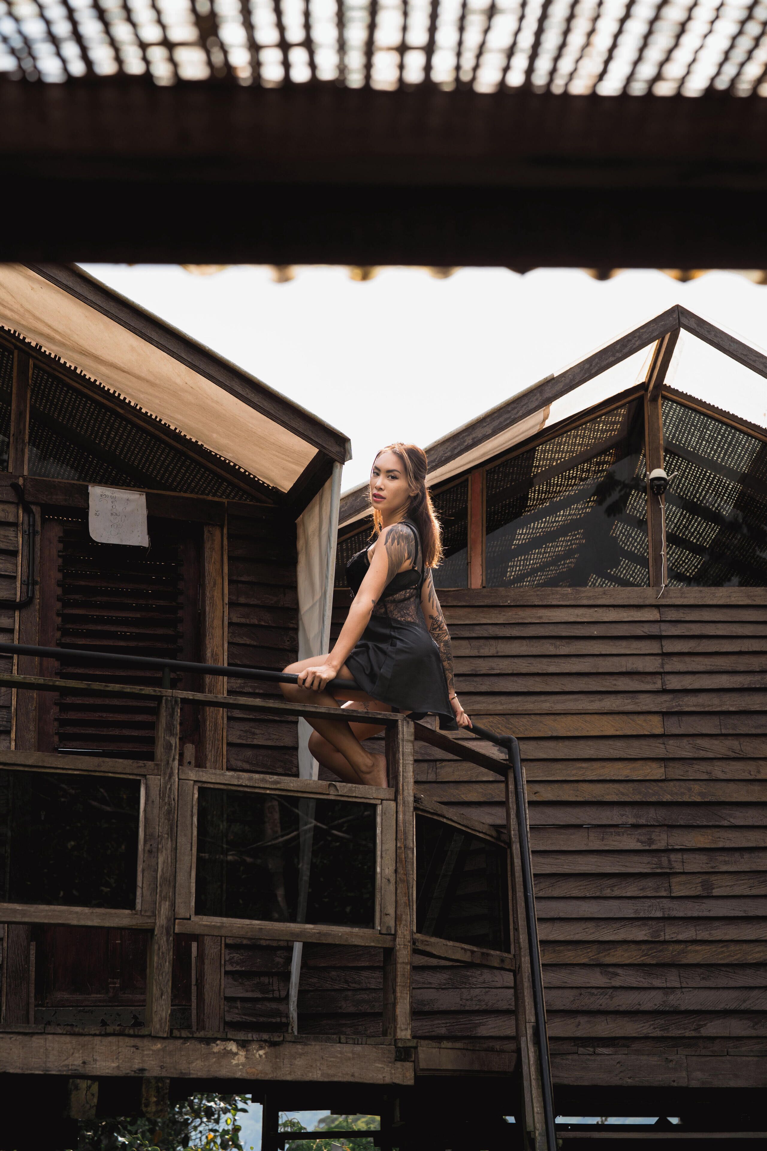 Une personne se tient sur un balcon en bois doté d’une rambarde en métal, d’où elle a une vue sur un bâtiment rustique en bois, avec de nombreuses fenêtres et un toit en pente.