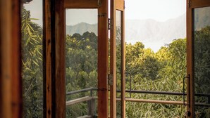 Ein Zimmer mit einer großen Glasdoor, die auf einen Balkon mit Blick auf einen üppigen Wald und Berge führt.