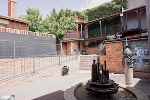 A courtyard with a fountain, a brick wall, and a balcony with a railing. - Palfreymans Arcade | Central NoHo 2 Bed Apartment - 2 (Hobart City)