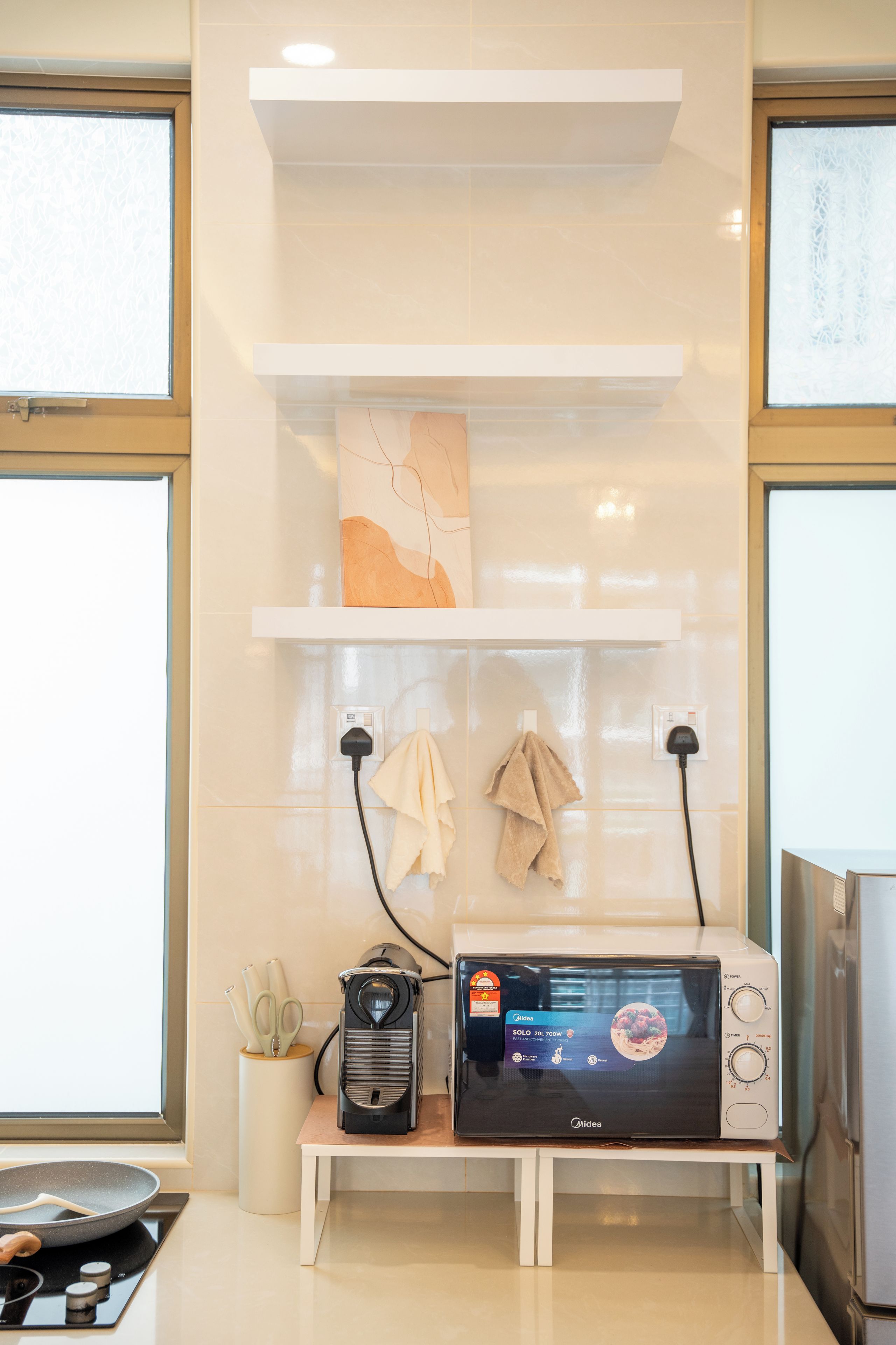 A kitchenette with a microwave, a kettle, and a frying pan on a stove.