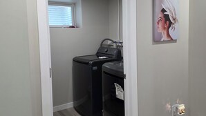 A laundry room with two washing machines, a ceiling light, and a small window.