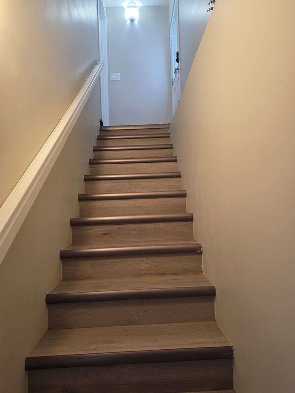 A wooden staircase with a handrail, leading to a landing with a light fixture.