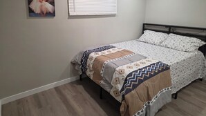 A bedroom with a bed, a window with blinds, a wall-mounted picture, and a wooden floor.