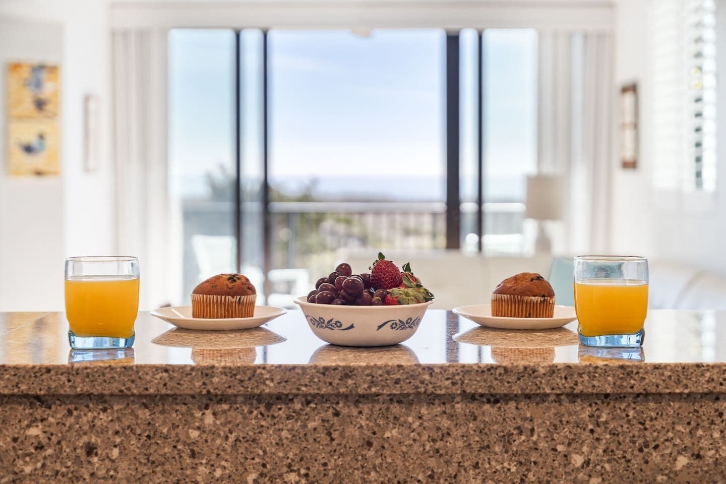 Desayuno con dos muffins, un tazón de fruta y dos vasos de jugo de naranja sobre una encimera de cocina.