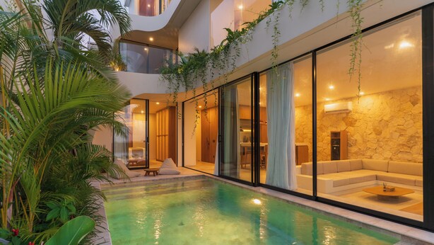 A modern indoor pool with clear water, surrounded by lush greenery and a stone wall. - Villa Kalani Soul by Alfred in Bali (Pecatu)
