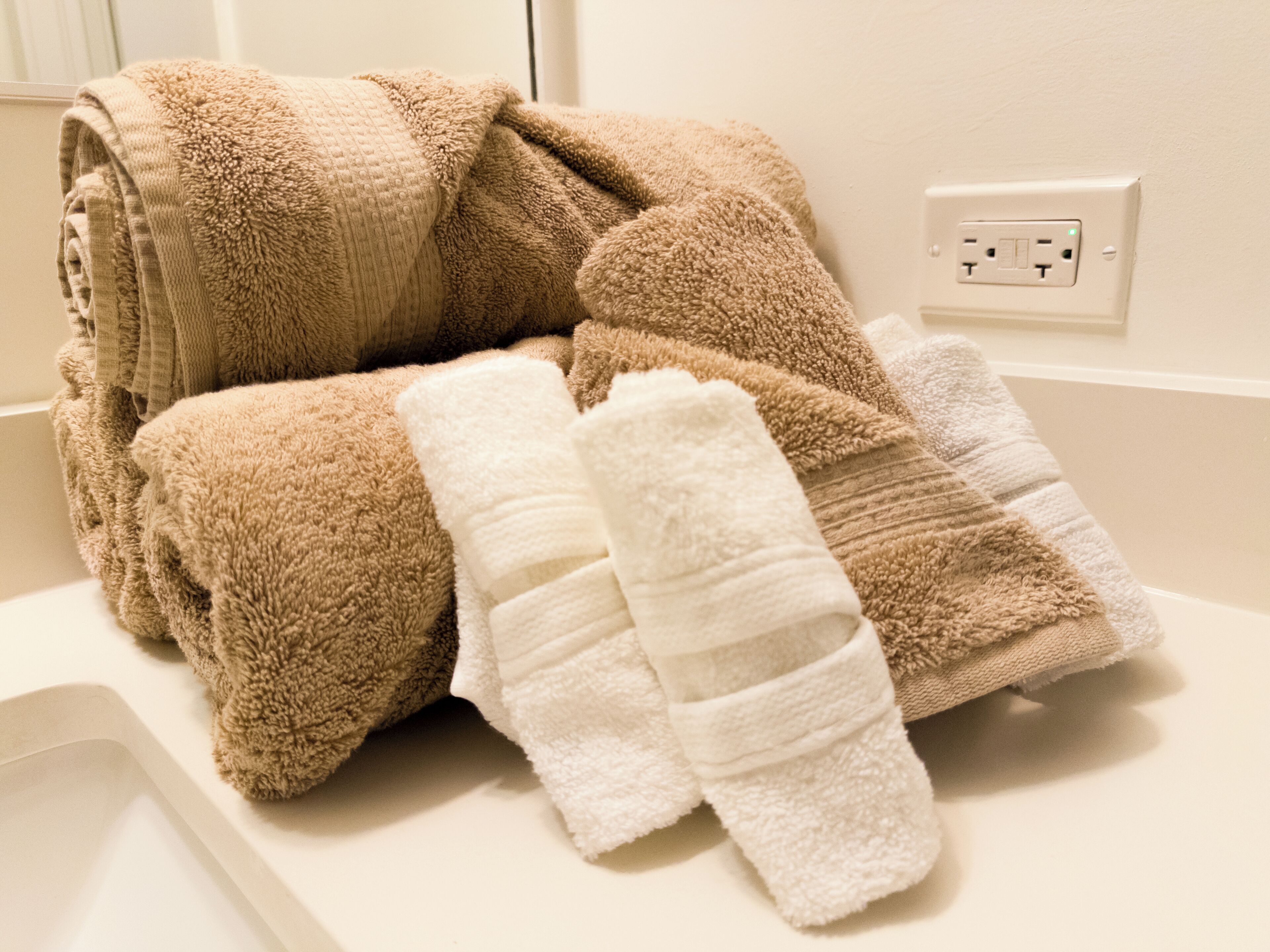 A bathroom with a white sink, a towel rack with folded towels, and a power outlet on the wall.