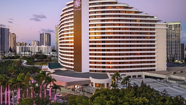 A modern hotel with a curved facade, multiple floors, and a prominent logo on the corner. - River View High-Rise 1BR Apartment by GC Casino (Broadbeach)