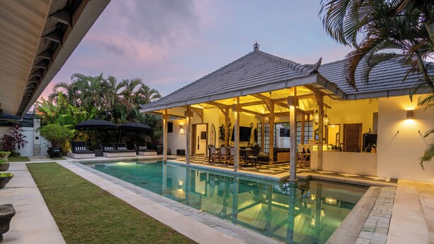 A swimming pool with a covered patio area, surrounded by a well-maintained lawn and palm trees. - Villa Luxe Bali 1 (Seminyak)