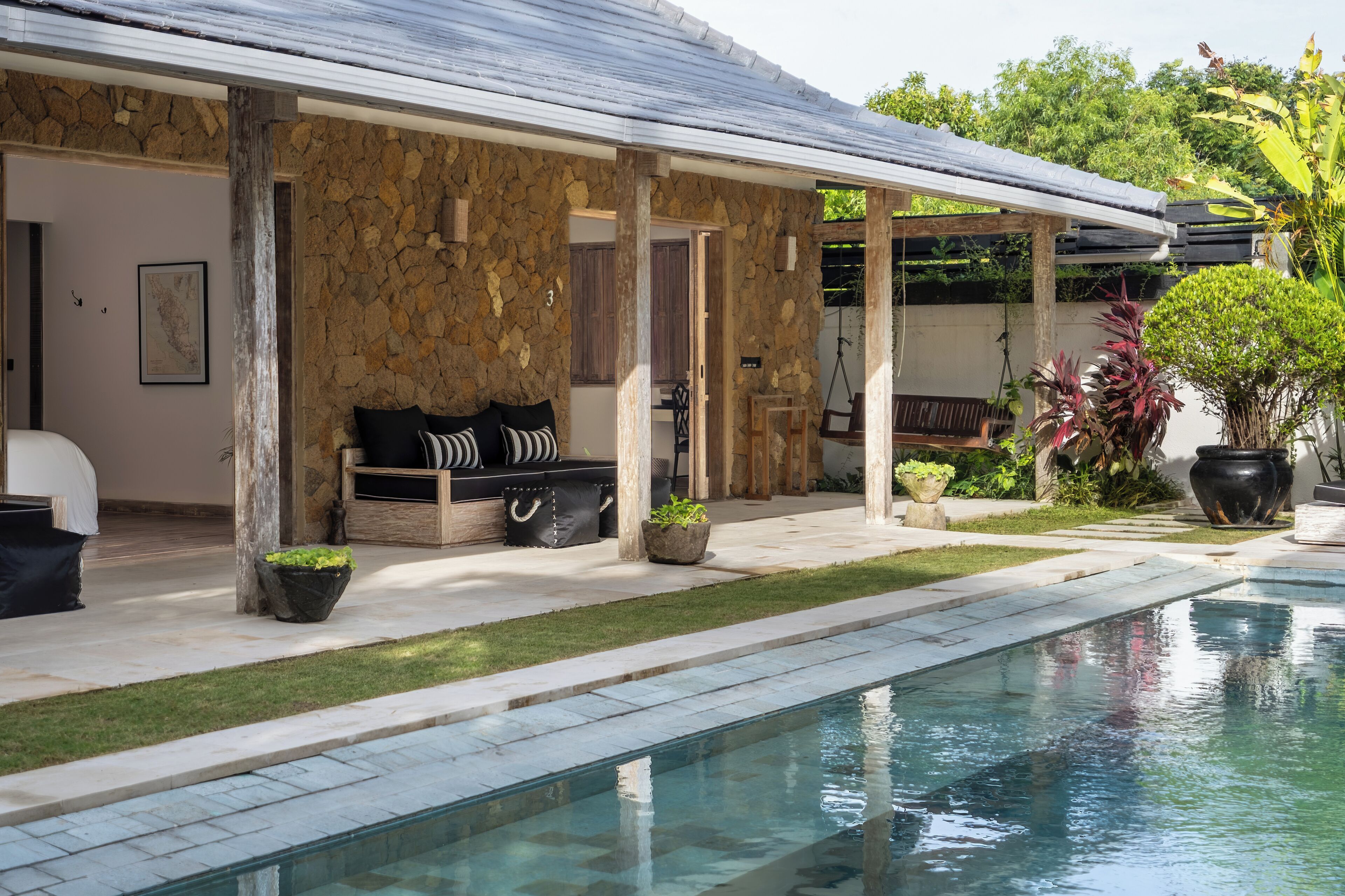 A poolside area with a stone wall, a covered seating area with a sofa, and a potted plant.