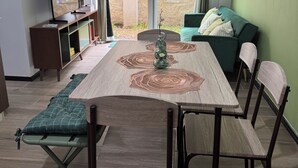 Comedor con mesa, sillas y vista a una pared de piedra a través de una puerta de vidrio.
