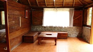 A rustic wooden room with a stone wall, a wooden bench, a table, and a window with a white curtain.