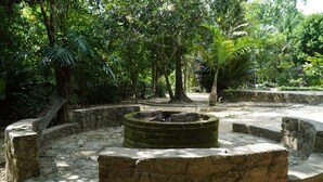 A stone fire pit surrounded by a stone wall in a lush garden with dense foliage.