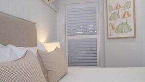 Ein Schlafzimmer mit einem Bett, Kissen, einer Wand-Klimaanlage, einem Fenster mit Jalousien und einem gerahmten Bild an der Wand.