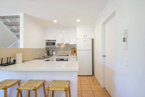 Une cuisine moderne avec des meubles blancs, un îlot central doté de tabourets, un four à micro-ondes et un réfrigérateur.
