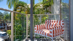 Ein Balkon mit einem weißen Metallstuhl, umgeben von üppiger Vegetation und freiem Blick auf die Straße.