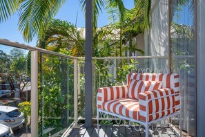 Ein Balkon mit einem weißen Metallstuhl, umgeben von üppiger Vegetation und freiem Blick auf die Straße.
