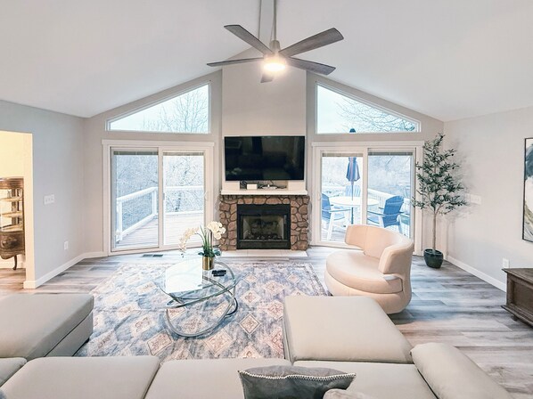 Un salón amplio con chimenea, ventilador de techo y ventanas grandes.