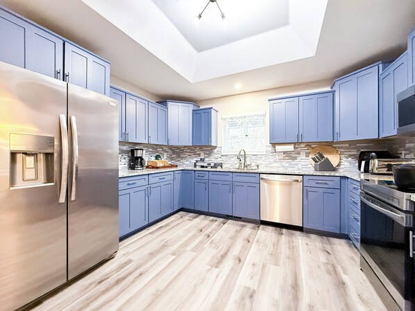 A modern kitchen with blue cabinets, stainless steel appliances, and a skylight. - Lakefront + Hot Tub + Dock + Backyard Trail Access + 2 Min to OZ Bike Park (Bella Vista)