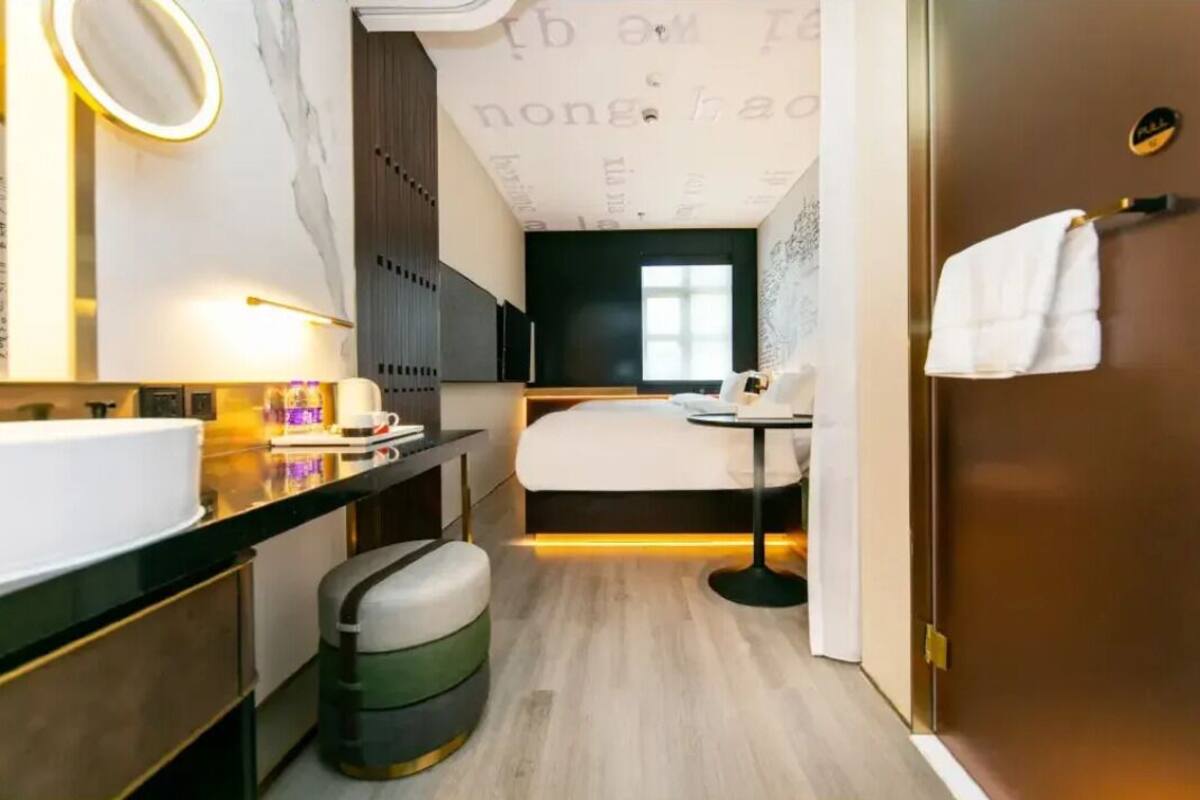 Ein modernes Hotelzimmer mit einem großen Bett, einem kleinen Tisch, einem runden Spiegel, einem Waschbecken und einem Mülleimer.