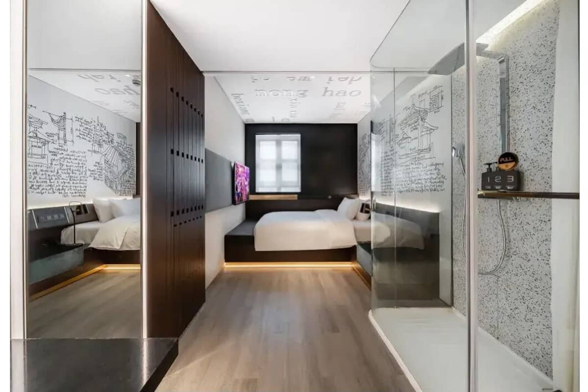 Ein modernes Hotelzimmer mit einem zentral platzierten Bett, einer kleinen Sitzecke und einem großen Fenster.