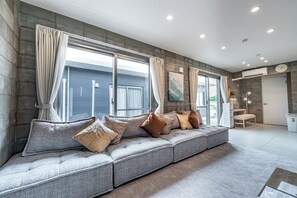 Een moderne woonkamer met een grijze modulaire bank, beige gordijnen en een groot raam.