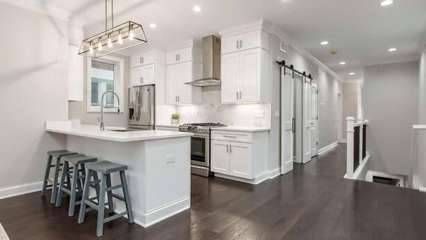 Cocina moderna con armarios blancos, una isla central con taburetes y una campana extractora de acero inoxidable.