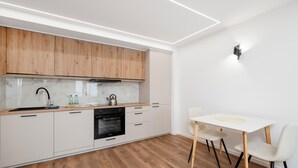 A modern kitchen with wooden cabinets, a built-in oven, and a dining area with a white table and chairs. - Piotrkowska Harmony Apartment (Łódź)