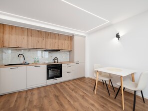 A modern kitchen with wooden cabinets, a built-in oven, and a dining area with a white table and chairs. - Piotrkowska Harmony Apartment (Łódź)
